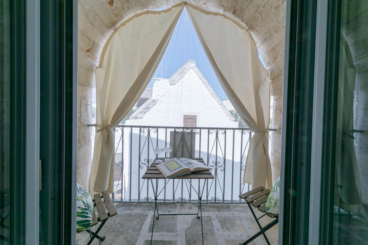 Una porta finestra aperta su un piccolo balcone con tavolino, e oltre la ringhiera i tetti del borgo
