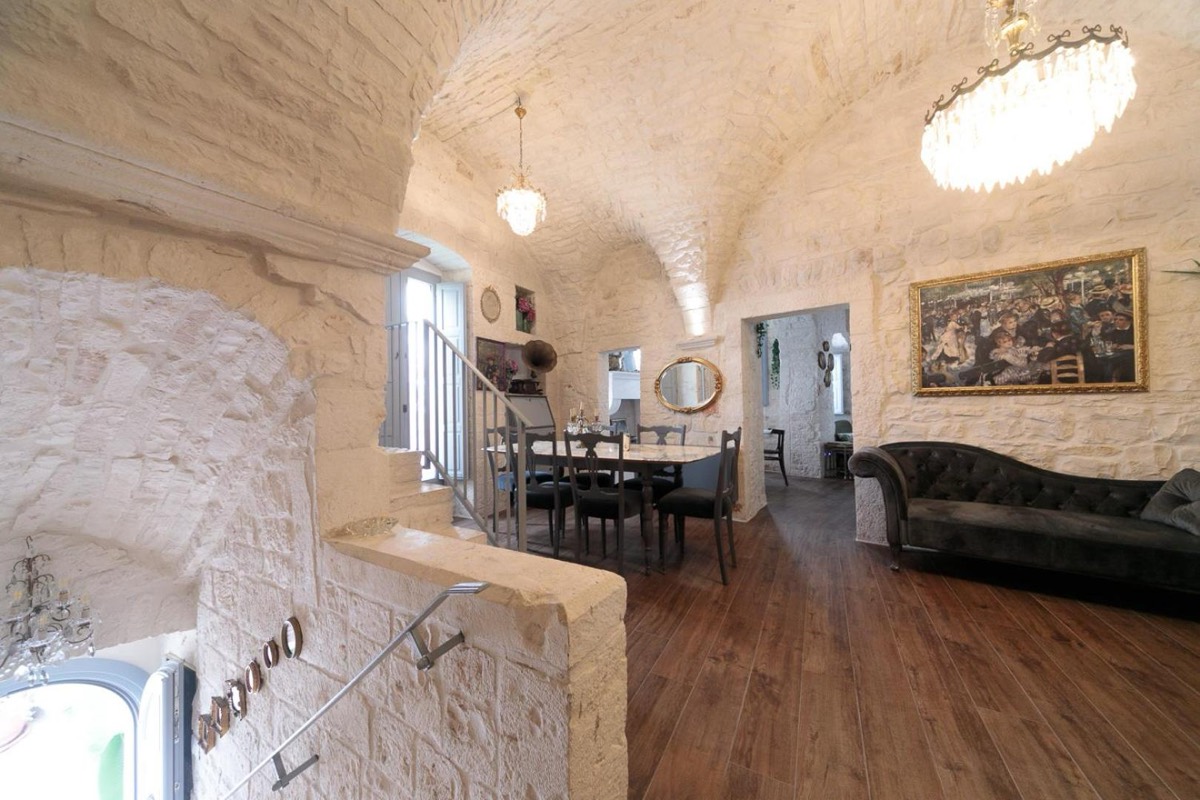 La sala comune di Operà sotto la volta in pietra imbiancata, con divano, lampadario e la scala che sale